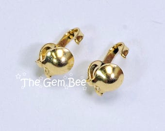 May include: Two gold-toned metal earring findings with a smooth, rounded dome shape and a curved clip-on mechanism. The text "The Gem Bee" is printed in white with small star outlines near the left earring finding on a plain white background.