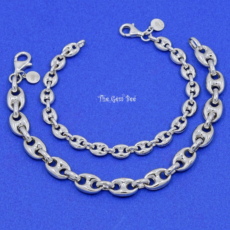 May include: Two silver-toned chain bracelets with a nautical link design. The bracelets are displayed on a blue background. One bracelet is larger than the other. The text "The Gem Bee" is visible.