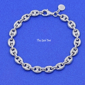 May include: A silver-colored bracelet with a puffed mariner chain design. The bracelet features a lobster clasp closure and a small charm. The Gem Bee text is visible on the blue background.