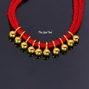 May include: A red string necklace with gold beads. The beads are round and have a smooth finish. The necklace is tied with a knot at the back.