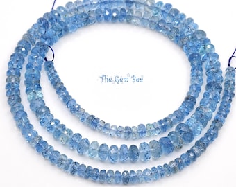 May include: A strand of faceted, light blue gemstone beads arranged in a circular pattern. The beads are translucent with a polished finish. The text "The Gem Bee" is printed in the center of the circular arrangement in a blue font.