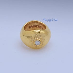 May include: A polished gold ring featuring a smooth, rounded band with a starburst engraving centered around a single clear, round-cut gemstone. The interior of the band is stamped with the text 14K G.M.I.K. The Gem Bee logo is visible in the corner.