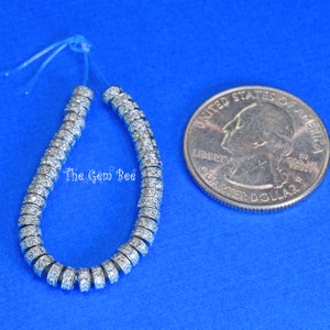 May include: A strand of silver beads with clear rhinestones, approximately the size of a UK 20 pence coin.