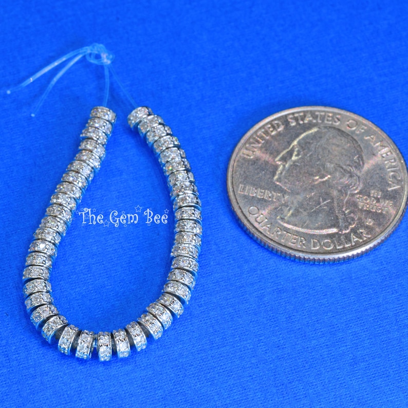 May include: A strand of silver beads with clear rhinestones, approximately the size of a UK 20 pence coin.