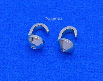 May include: Two silver-toned metal cord ends with a rounded, conical base and a curved hook attachment. The components feature a smooth, reflective finish and are positioned side-by-side. The text The Gem Bee is visible above the items.