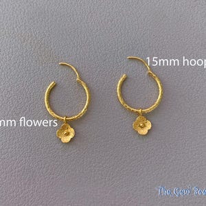 Puede incluir: Un par de pendientes de aro dorados con acabado texturizado, cada uno con un dije de flor de 6mm. Los aros miden 15mm de di&aacute;metro. El texto 15mm hoops y 6mm flowers es visible, junto con la marca The Gem Bee en la esquina inferior.