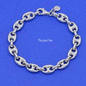 May include: A silver-toned, polished link bracelet with a lobster clasp closure. The links are oval-shaped with a rounded, hollowed-out center. The Gem Bee is printed on the blue background.