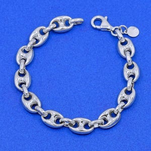 May include: A silver-colored bracelet with a series of oval-shaped links, connected to form a chain. The bracelet has a lobster clasp closure and a small, round charm. The background is a solid blue.
