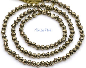 May include: A strand of faceted, metallic gold-toned pyrite beads arranged in a circular pattern with a green thread tassel at the top. The text The Gem Bee is printed in blue in the center of the beads, featuring small star icons.