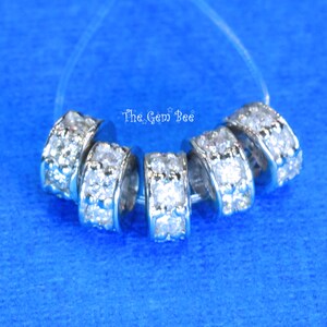 May include: Six silver-toned spacer beads with clear rhinestones. The beads are arranged in a circle on a blue background.
