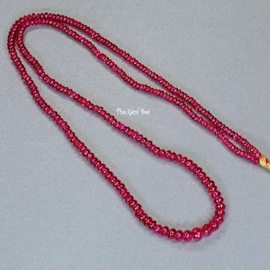 Peut inclure: Un long collier composé de petites perles rondes de rubis rouges. Le collier est enfilé sur un fil d'or et possède un petit fermoir en or.
