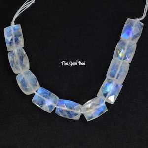 May include: A strand of white moonstone beads with iridescent blue and green flashes. The beads are rectangular and faceted, and they are strung on a white cord.