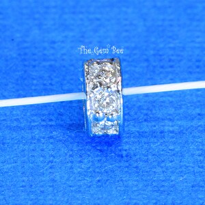 May include: Silver spacer bead with a row of clear cubic zirconia stones around the edge. The bead is on a white string.