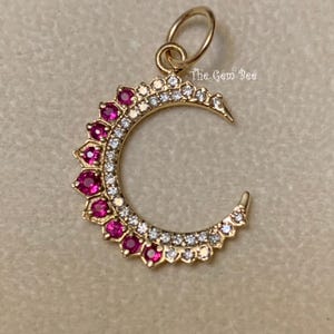 May include: A gold crescent moon pendant featuring a row of small clear white stones along the inner curve and a row of vibrant pink stones set in petal-like frames along the outer edge. The pendant includes a circular bail and the text The Gem Bee.