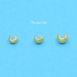 May include: Three gold-coloured metal crimp beads, each with a rounded shape and a small opening. The beads are arranged in a row on a blue background.