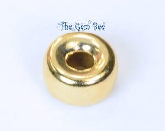 May include: A small, round, gold-colored metal bead with a smooth, reflective surface and a central hole. Above the bead, the text The Gem Bee is printed in blue with small star accents, identifying the source of this jewelry component.