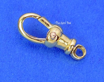 May include: A gold-toned metal lobster claw clasp featuring a spring-loaded mechanism and a small circular loop at the base. The surface is smooth and reflective. The text The Gem Bee is printed in small white letters near the center of the clasp.