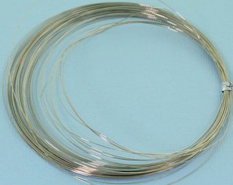 May include: A continuous coil of thin, flexible silver-colored metal wire arranged in a circular loop. The wire has a smooth, reflective surface and is held together by a small, rectangular silver-colored metal fastener on the right side.