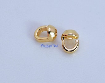 May include: Two small, shiny gold-toned metal crimp covers with a smooth, rounded dome shape and a C-shaped opening. The text The Gem Bee is printed in blue between the two pieces. These jewelry findings are designed to conceal crimp beads.