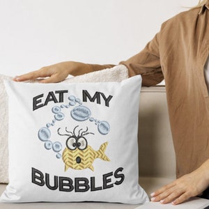 May include: White pillow with embroidered text "Eat My Bubbles" and a cartoon fish blowing bubbles. The fish is yellow with black eyes and a surprised expression.