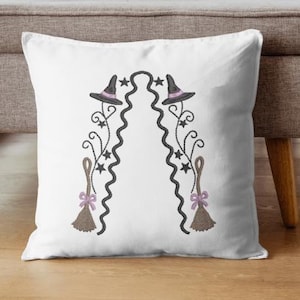 May include: A white square throw pillow featuring a centered embroidery design of two witch hats, two brooms with light purple bows, and black swirling lines accented with small black stars arranged in a symmetrical arch pattern.