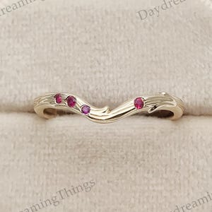 May include: A gold-colored ring with a curved design, featuring three small, round, red gemstones. The ring is set in a beige velvet ring box. The text "Daydreaming Things" is visible.