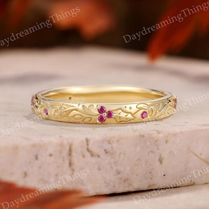May include: A gold band ring featuring an engraved botanical leaf pattern and small, round, pinkish-red gemstones set into the metal. The ring has a polished finish and displays the text DaydreamingThings overlaid across the image.