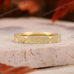 Op de afbeelding: Een goudkleurige ring met een geometrisch patroon van ruiten en sterren. De ring ligt op een lichtgekleurd oppervlak. De tekst "Daydreaming Things" is zichtbaar op de achtergrond.