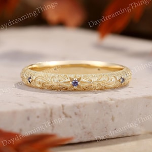 Puede incluir: Un delicado anillo de banda de oro con un diseño grabado intrincado y pequeñas piedras preciosas azules.