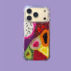 Puede incluir: Funda transparente para teléfono con un diseño de frutas con cuentas. El diseño incluye una fruta del dragón, aguacate, papaya y sandía. Las frutas son de varios colores, incluyendo rosa, verde, rojo, naranja y amarillo. La funda del teléfono tiene una parte trasera dorada.
