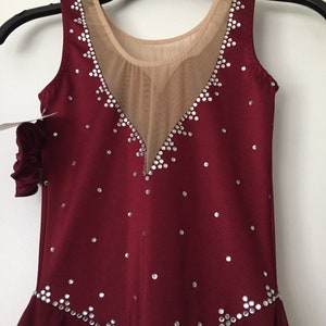 Puede incluir: Vestido de patinaje burdeos sin mangas con un panel de malla transparente y adornos de pedrer&iacute;a plateada.