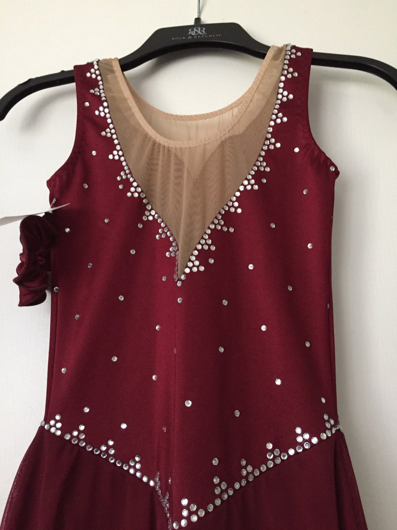 Puede incluir: Vestido de patinaje burdeos sin mangas con un panel de malla transparente y adornos de pedrer&iacute;a plateada.