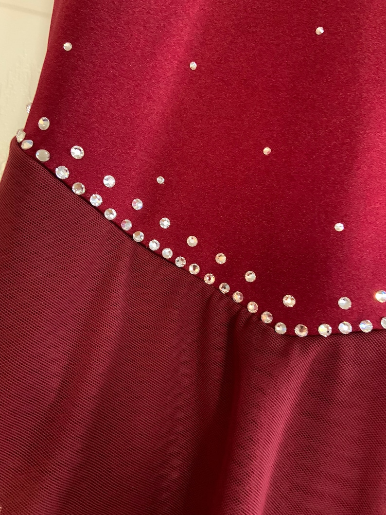 May include: A burgundy dance leotard with a mesh skirt and a line of rhinestones around the waist.