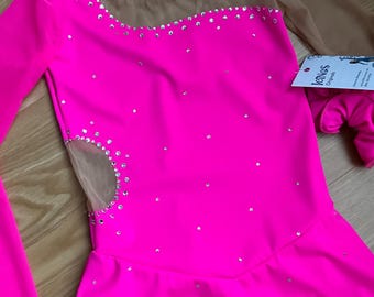 Puede incluir: Vestido de patinaje artístico rosa brillante con mangas largas y escote transparente. El vestido está adornado con pedrería y presenta un detalle de corte en el lateral. Se incluye un guante rosa a juego. La etiqueta dice "Icings Originals".