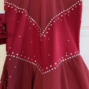 May include: Burgundy figure skating dress with a sheer overlay and a V-shaped design of rhinestones.