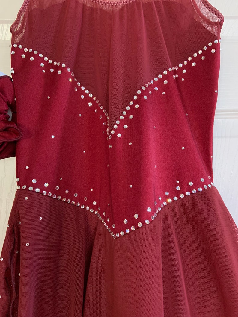 May include: Burgundy figure skating dress with a sheer overlay and a V-shaped design of rhinestones.