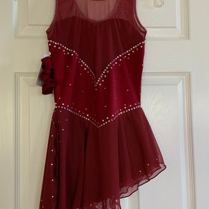 May include: Burgundy figure skating dress with a sheer bodice and a layered skirt. The dress is decorated with rhinestones.