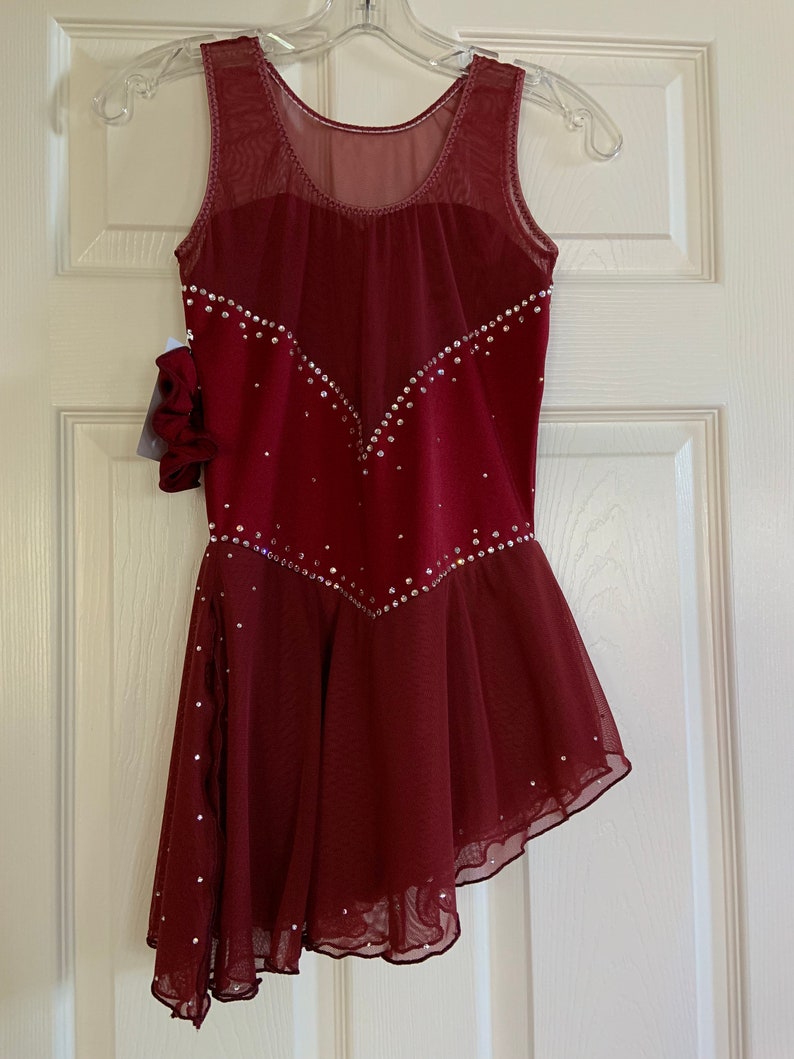 May include: Burgundy figure skating dress with a sheer bodice and a layered skirt. The dress is decorated with rhinestones.