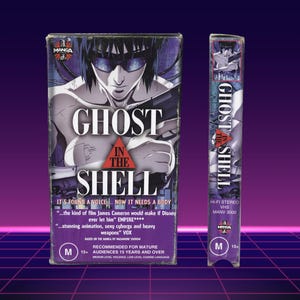 Może przedstawiać: Kaseta VHS z filmem "Ghost in the Shell" z ilustracją w stylu mangi przedstawiającą postać w okularach przeciwsłonecznych i z bronią. Na kasecie znajdują się napisy, w tym "Manga" i "Hi-Fi Stereo VHS".