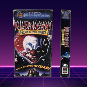 May include: A VHS tape for the movie "Killer Klowns From Outer Space" with a colorful clown face on the cover. The tape is black with the title and "VHS" printed on the spine. The tagline reads "In space no one can eat ice cream!"