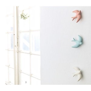 May include: Three ceramic bird wall hooks in pink, blue, and white. The birds are in a flying position with their wings spread out.