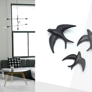 May include: Three black ceramic swallow wall sculptures in flight. The swallows are in various positions, with their wings spread out. The sculptures are on a white background.