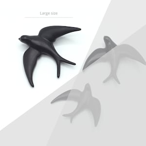 May include: Three black ceramic swallow bird wall decor. The large swallow is in focus and the two smaller swallows are blurred in the background.  The text "Large size" is at the top of the image.