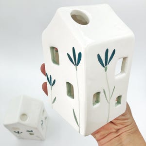 May include: Two white ceramic houses with cut-out windows and blue floral designs. The houses are painted with green stems and leaves.