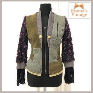 May include: A green, brown and grey patchwork jacket with a black zip and gold buttons. The sleeves are made of a fuzzy, pink and black fabric. The jacket has a collar and a fitted silhouette.