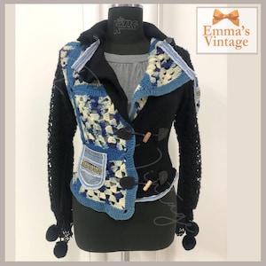 Może przedstawiać: Czarna dzianinowa kurtka z niebieskimi i białymi panelami z dzianiny, akcentami z dżinsu i drewnianymi zapięciami. Kurtka ma długie rękawy z czarnymi pomponami przy mankietach.