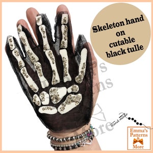 Può includere: Un guanto per mano scheletro in tulle nero con strass. Il guanto è sulla mano di una persona. Il testo "Skeleton hand on cutable black tulle" è nell'angolo in alto a destra dell'immagine. Il testo "Emma's Patterns & More" è nell'angolo in basso a destra dell'immagine.