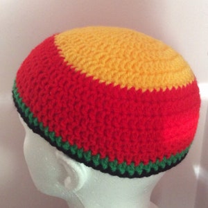 May include: A round, crocheted beanie hat featuring horizontal bands of color. The top section is bright yellow, followed by a wide band of red, a thinner band of green, and a narrow black border along the bottom edge of the headwear.