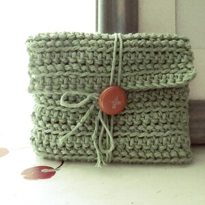May include: A green knitted pouch with a button closure and a tied string. The pouch is made of a soft, textured yarn.