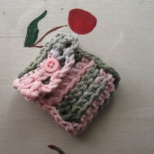 May include: A crocheted pink and green washcloth with a pink button in the center.
